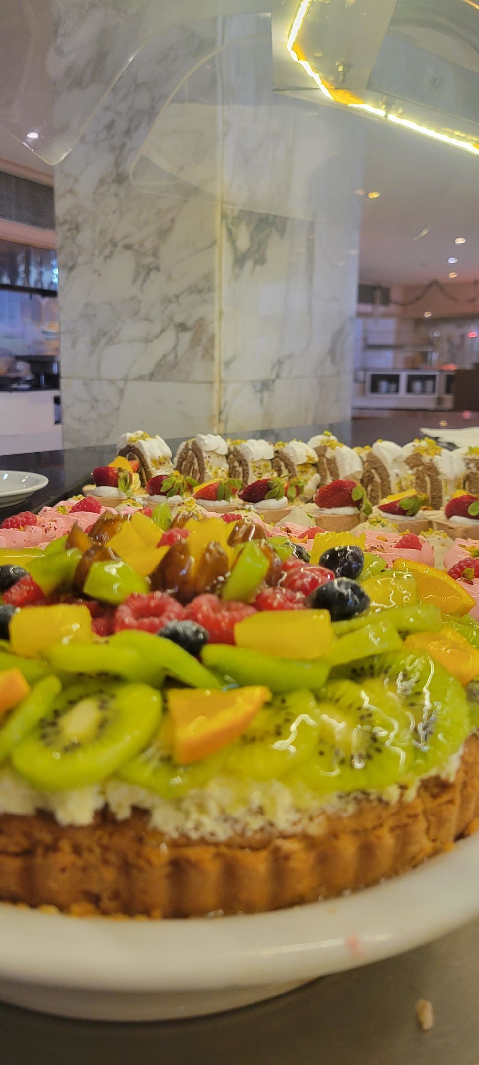 A dessert platter with various fruits and cream on a white plate, set against a marble background.