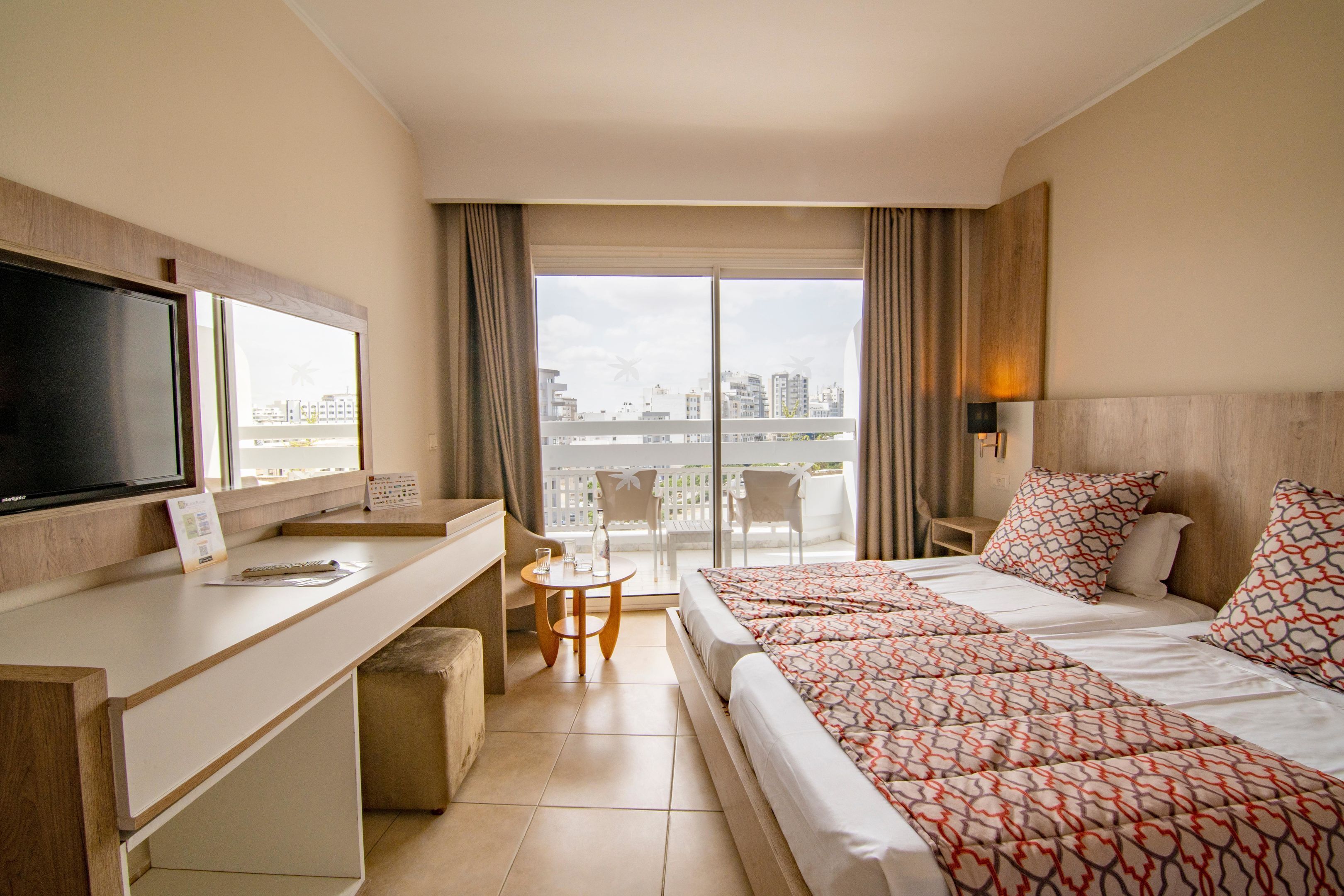 Une chambre d’hôtel avec un lit, un bureau et un balcon donnant sur la ville.