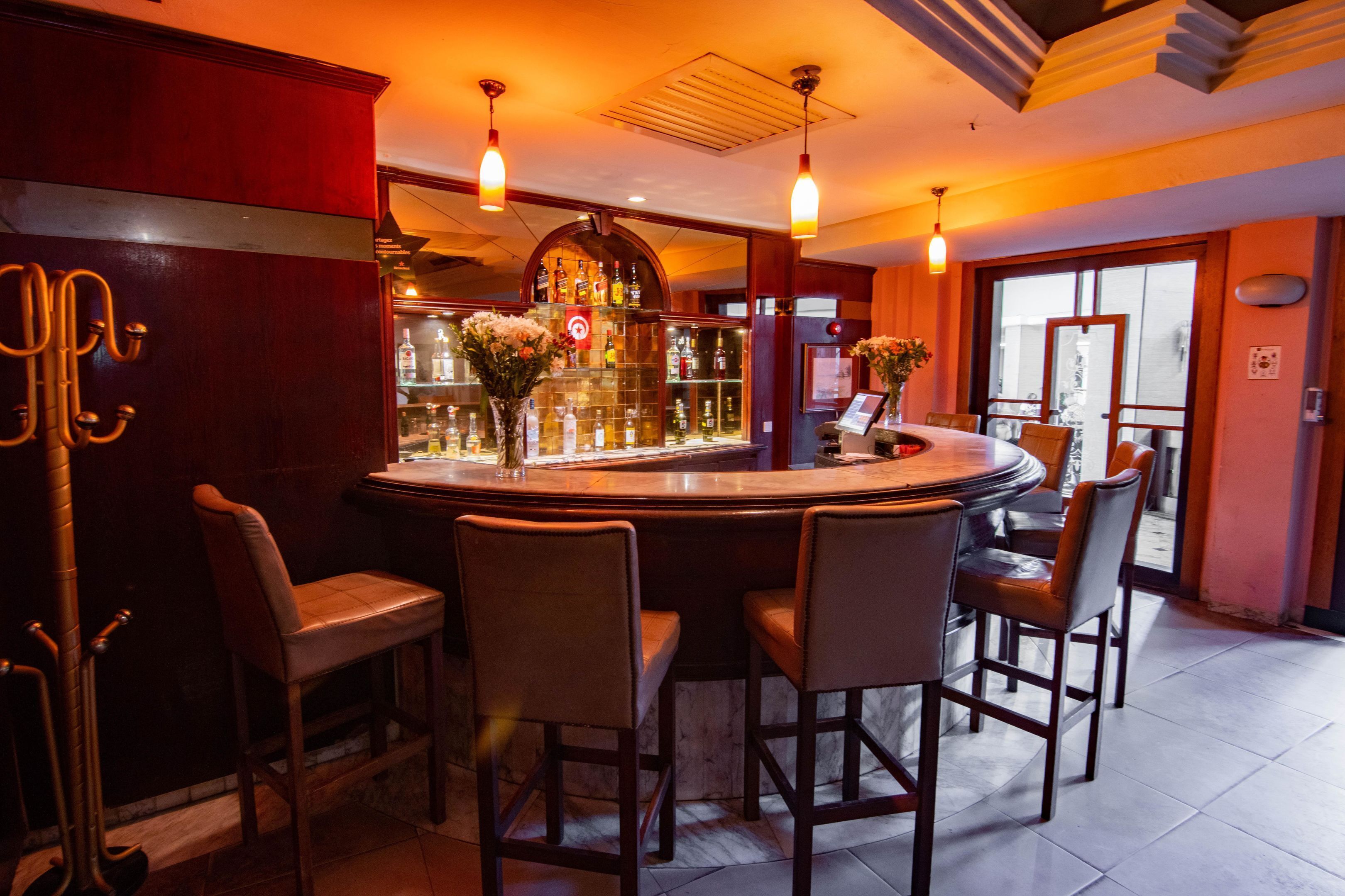 Una zona de bar con una mesa redonda, taburetes de bar y una vitrina de vidrio con botellas.