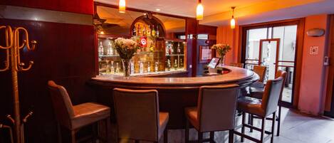 Una zona de bar con una mesa redonda, taburetes de bar y una vitrina de vidrio con botellas.