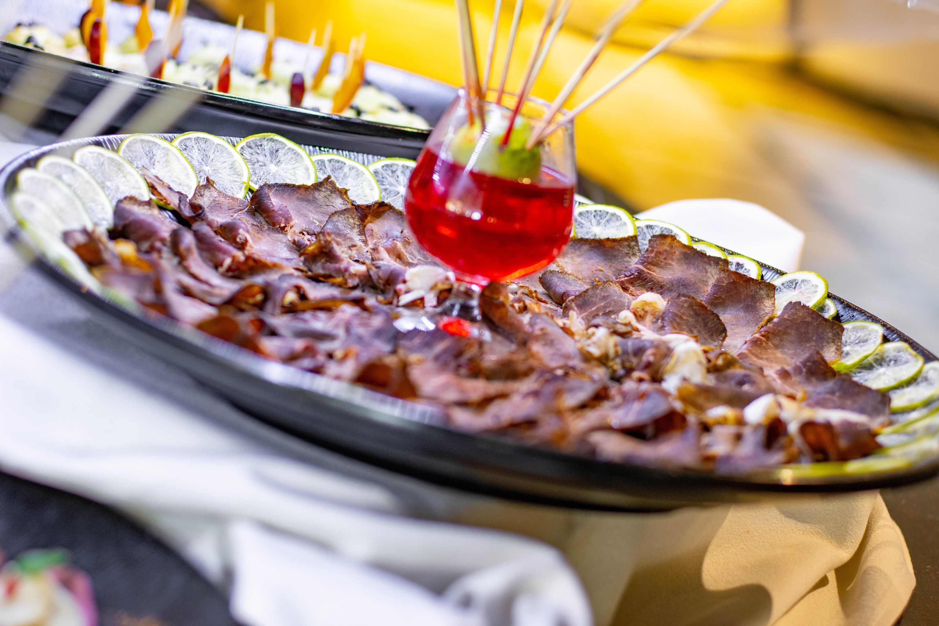 A plate of thinly sliced meat with lime wedges and a red drink garnish.