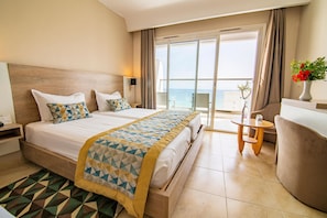 A hotel room with a large bed, a small table, and a view of the sea through a sliding door.