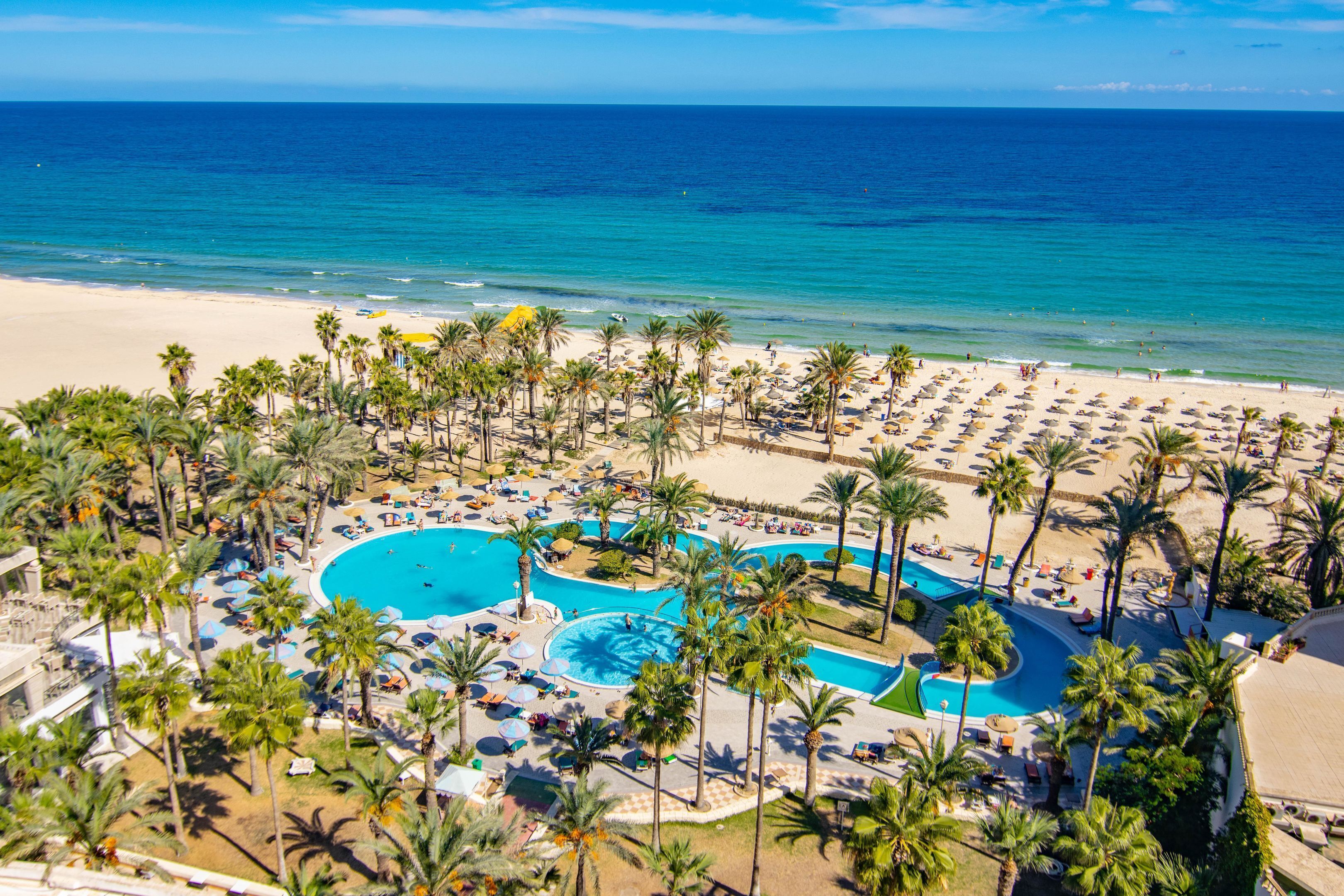 A resort with a large pool, palm trees, and a beach.