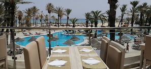 A poolside view with a clear view of the ocean, palm trees, and a lounge area with tables and chairs. - Riadh Palms Resort & Spa (Sousse)