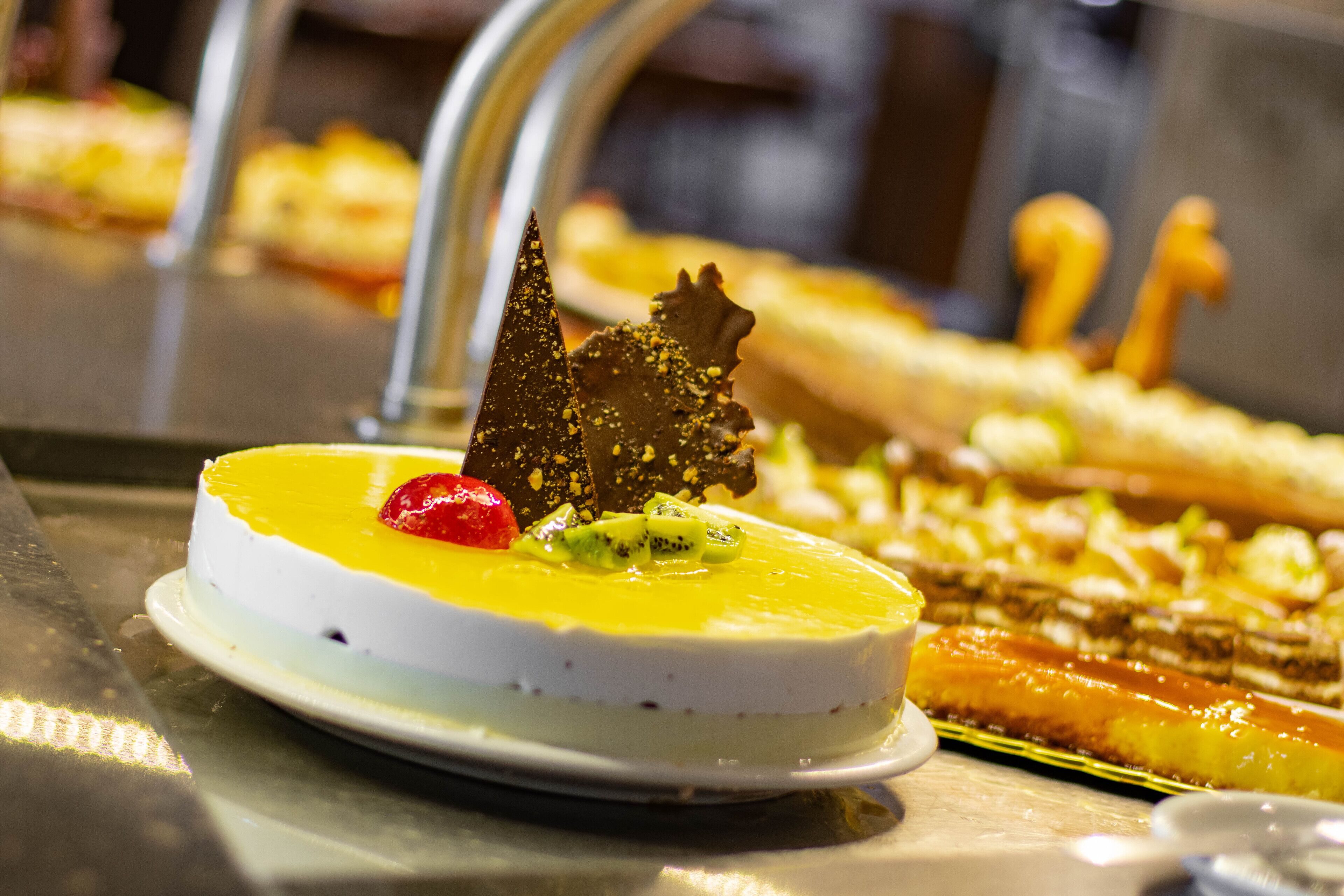 A dessert plate with a white base, yellow topping, kiwi slices, and a chocolate piece.