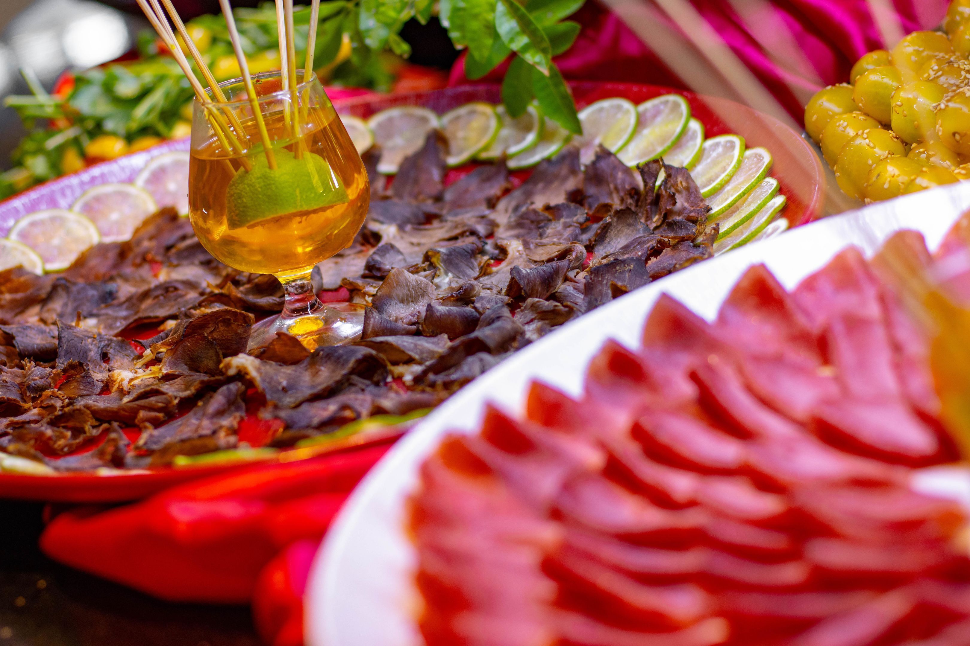 A variety of food items including a plate with sliced meat, a glass with a drink, and garnishes like lime slices and herbs.