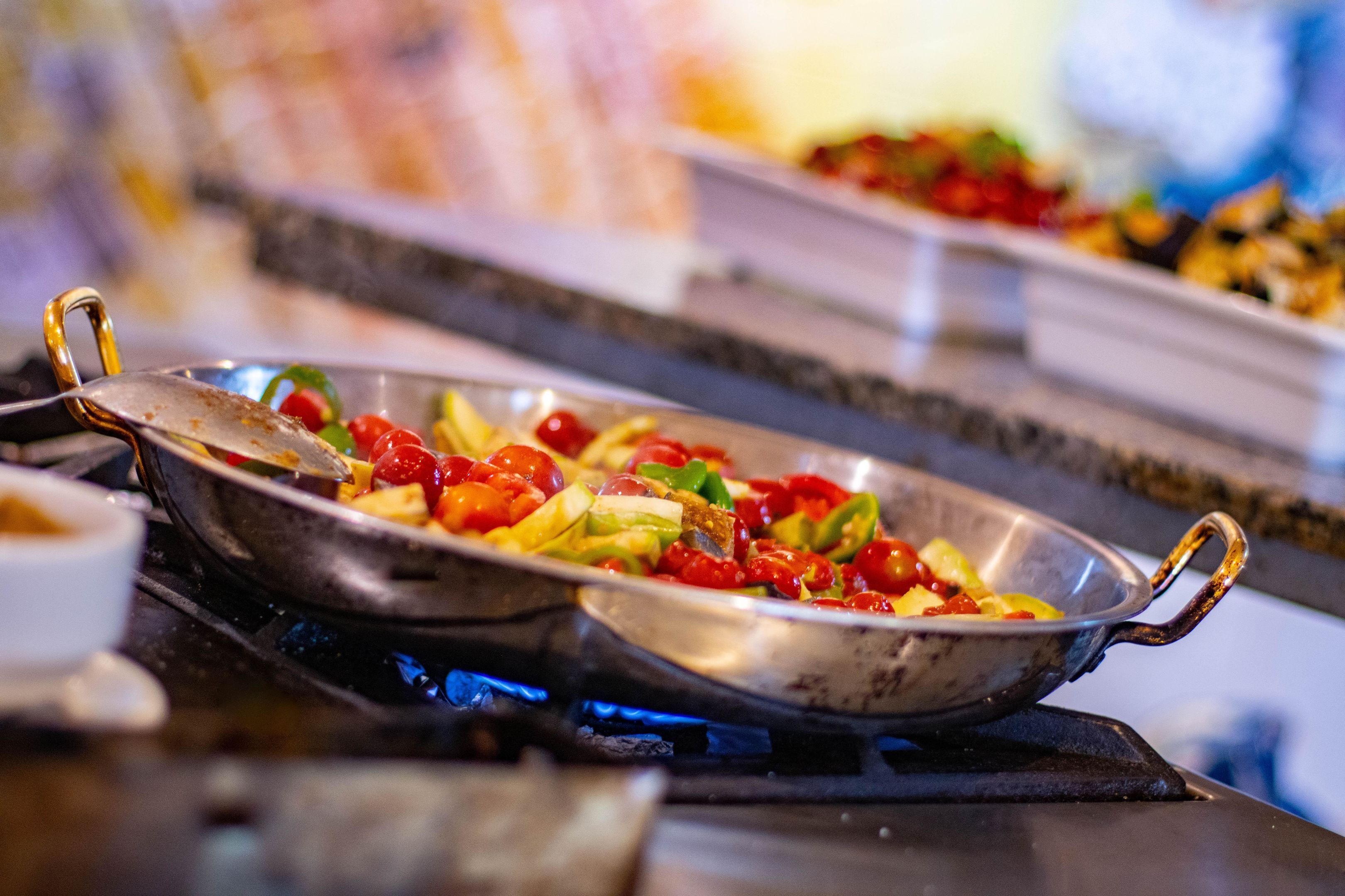A buffet with a variety of dishes, including a pan of vegetables and a bowl of fruit.