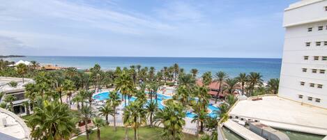 Un resort con piscina rodeada de palmeras, una playa y vista al océano.
