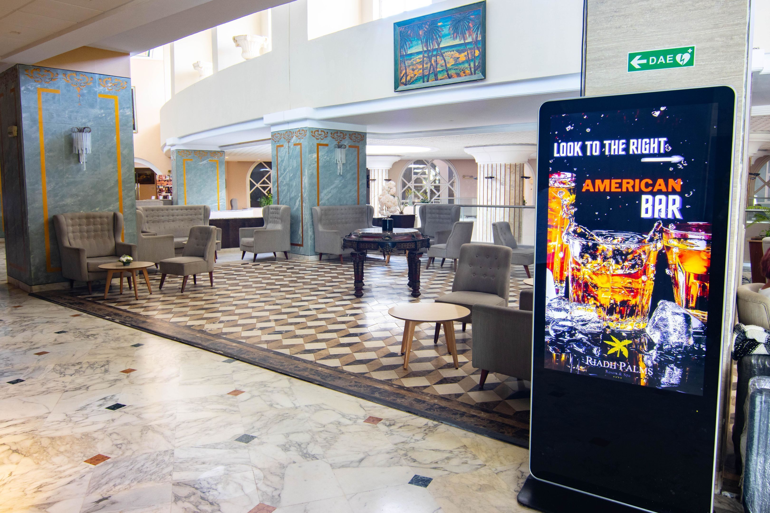 A lobby with a checkered floor, seating area, and a digital sign promoting the American Bar.