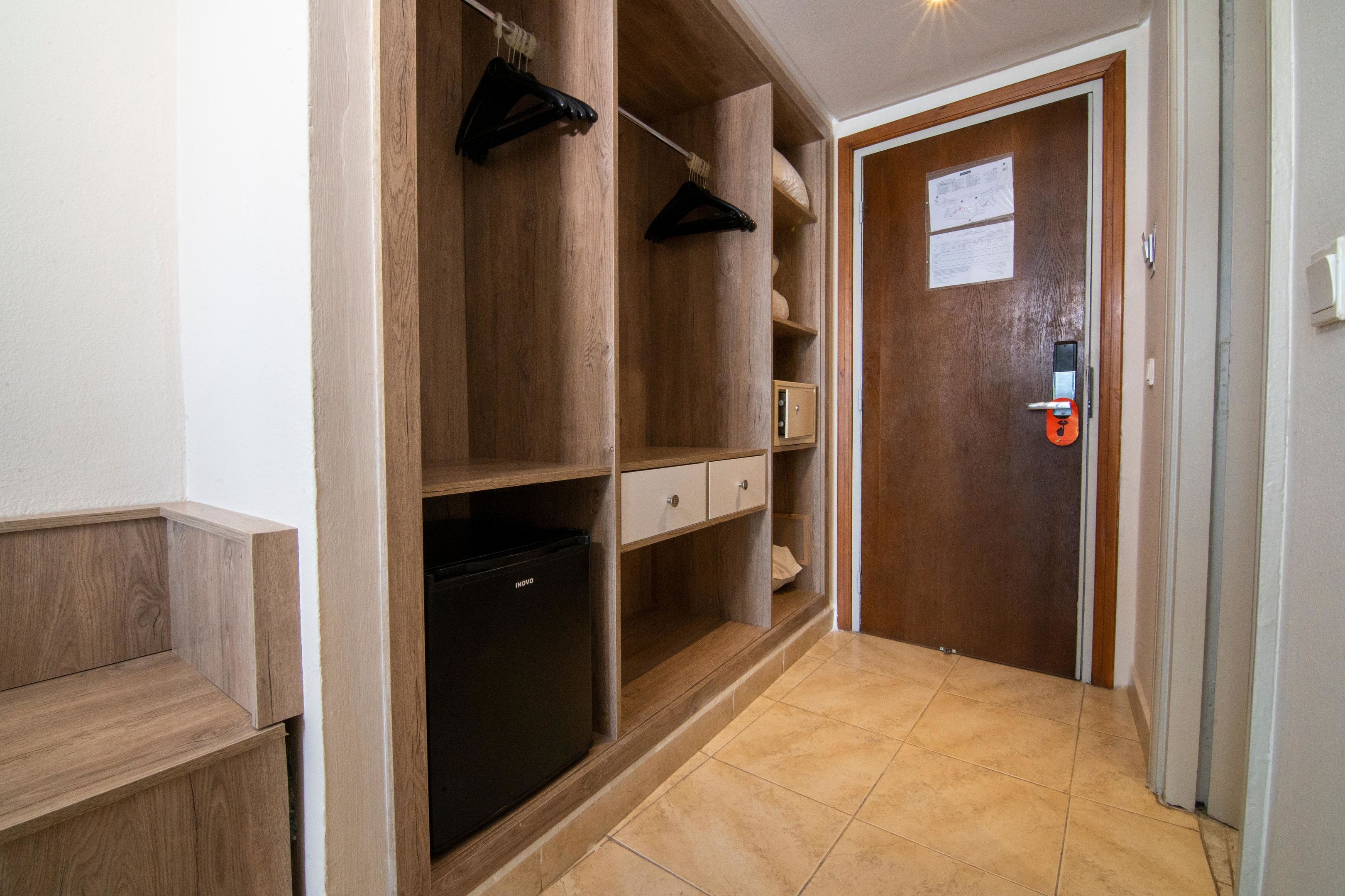 Ein Flur mit Holzregalen, einem schwarzen Kühlschrank und einer Tür mit Sicherheitsschloss.