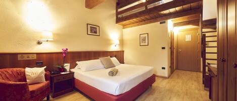 A hotel room with a wooden ceiling, a bed with white bedding, a red sofa, a nightstand with a lamp, and a wooden wardrobe.