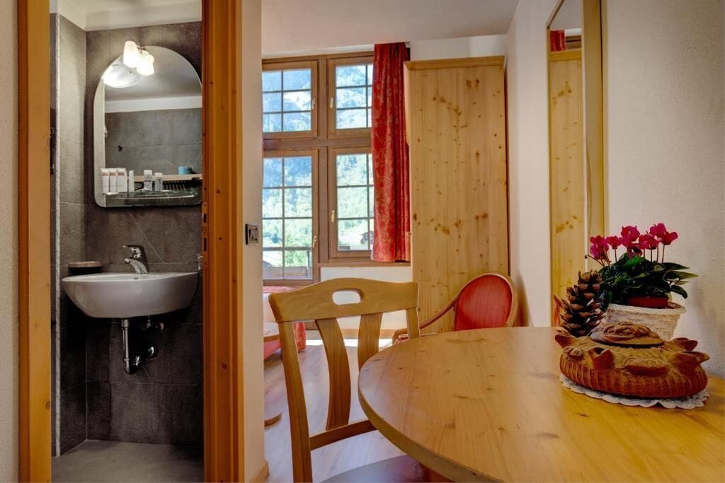 Een badkamer met een wastafel en spiegel, een houten eettafel met stoelen en een raam met gordijnen.