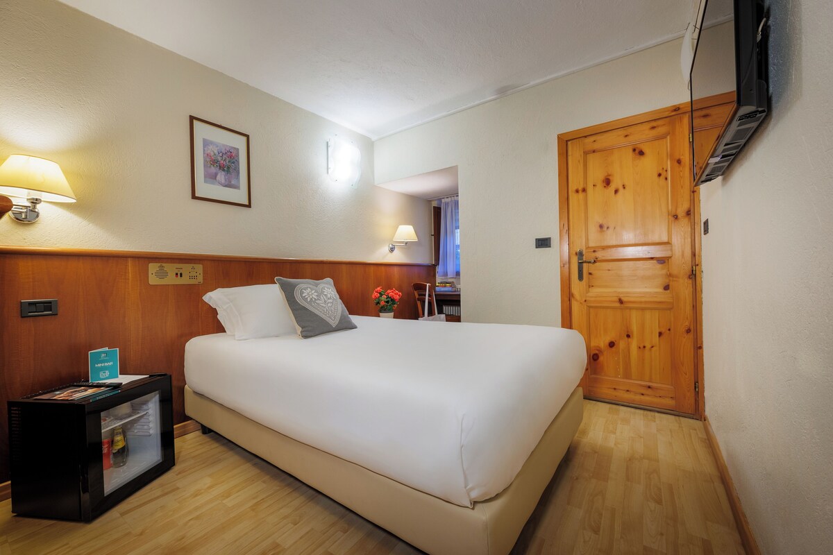 A hotel room with a bed, a nightstand, a TV, and a wooden door.