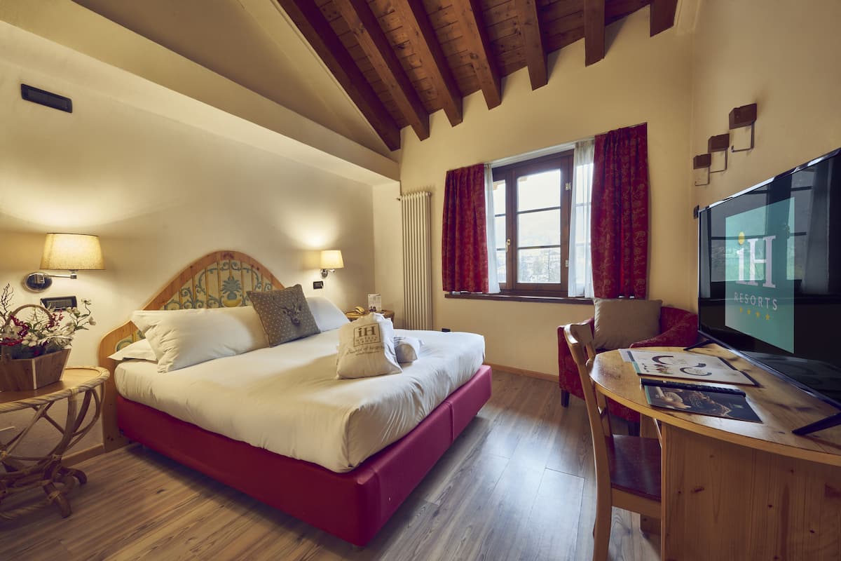 A bedroom with a bed, bedside tables, a desk, and a television.