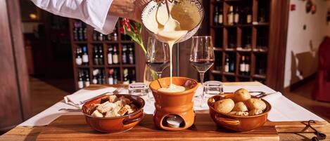 A person pouring a creamy substance into a bowl, with wine glasses and a wooden table in the background.