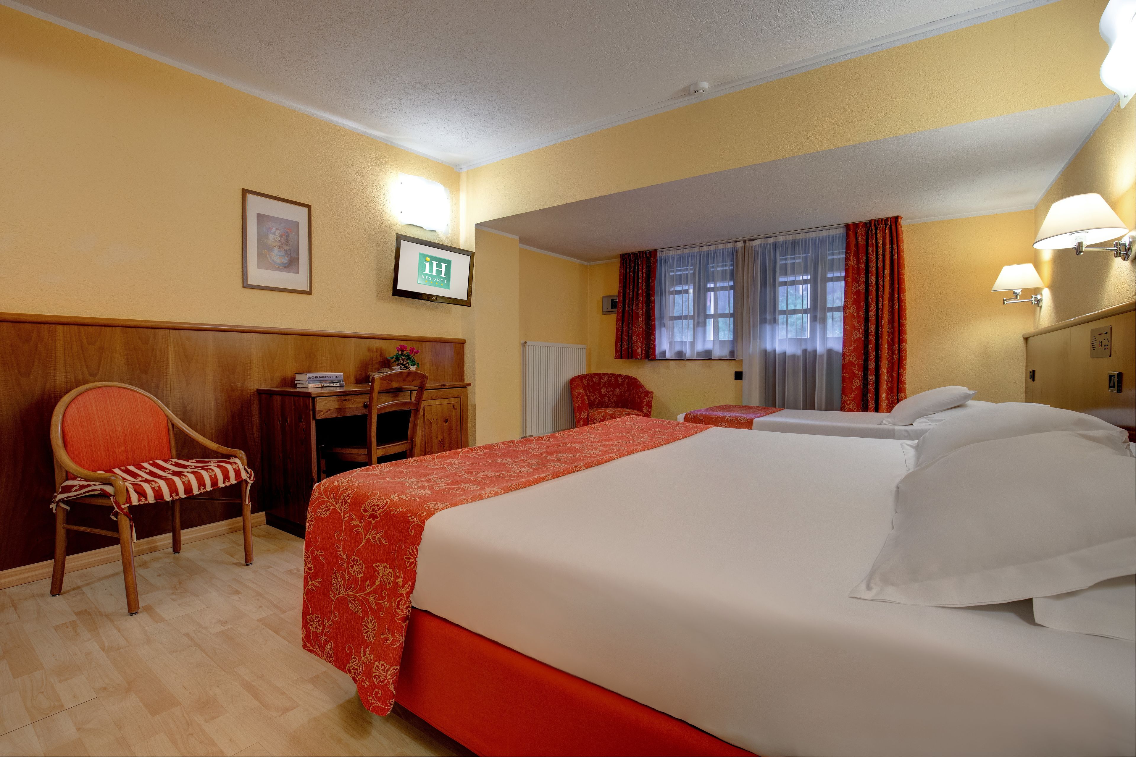 Habitación de hotel con dos camas, una silla de madera, un escritorio y una ventana con cortinas.