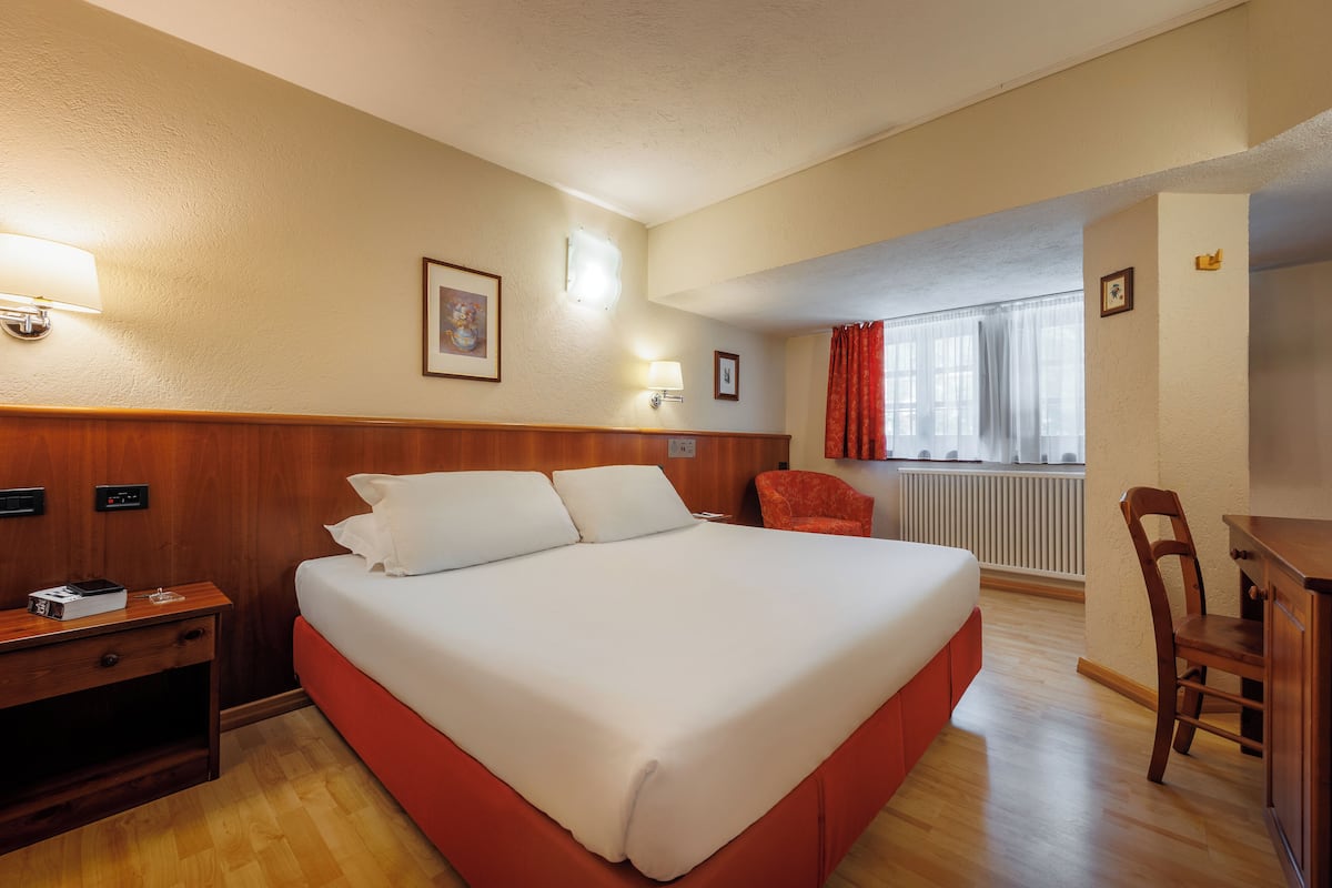 A hotel room with a large bed, wooden headboard, a desk, and a chair.