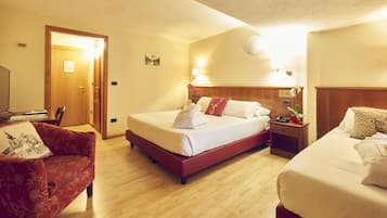Ein Hotelzimmer mit einem großen Bett, einem kleineren Bett, einem roten Sessel, einem hölzernen Nachttisch und einem Schreibtisch mit einer Lampe.