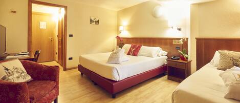 A hotel room with a large bed, a smaller bed, a red armchair, a wooden nightstand, and a desk with a lamp.
