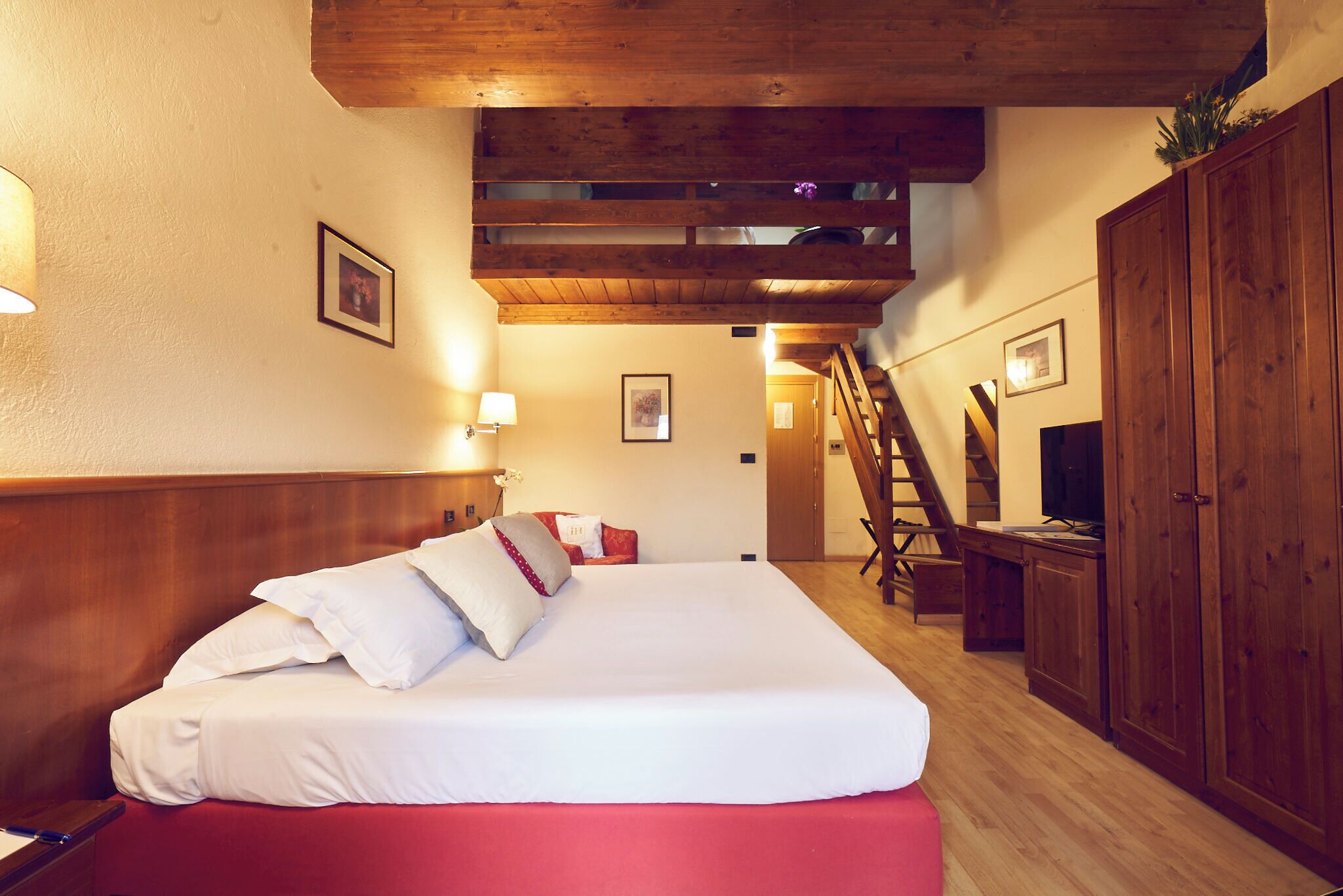 Ein Hotelzimmer mit Bett, Holz-Kopfteil, einer Treppe und einem Kleiderschrank.