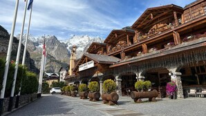 A hotel with a wooden facade, balconies with flower boxes, and a mountain backdrop. - IH Hotels Courmayeur Mont Blanc Resort (Courmayeur)