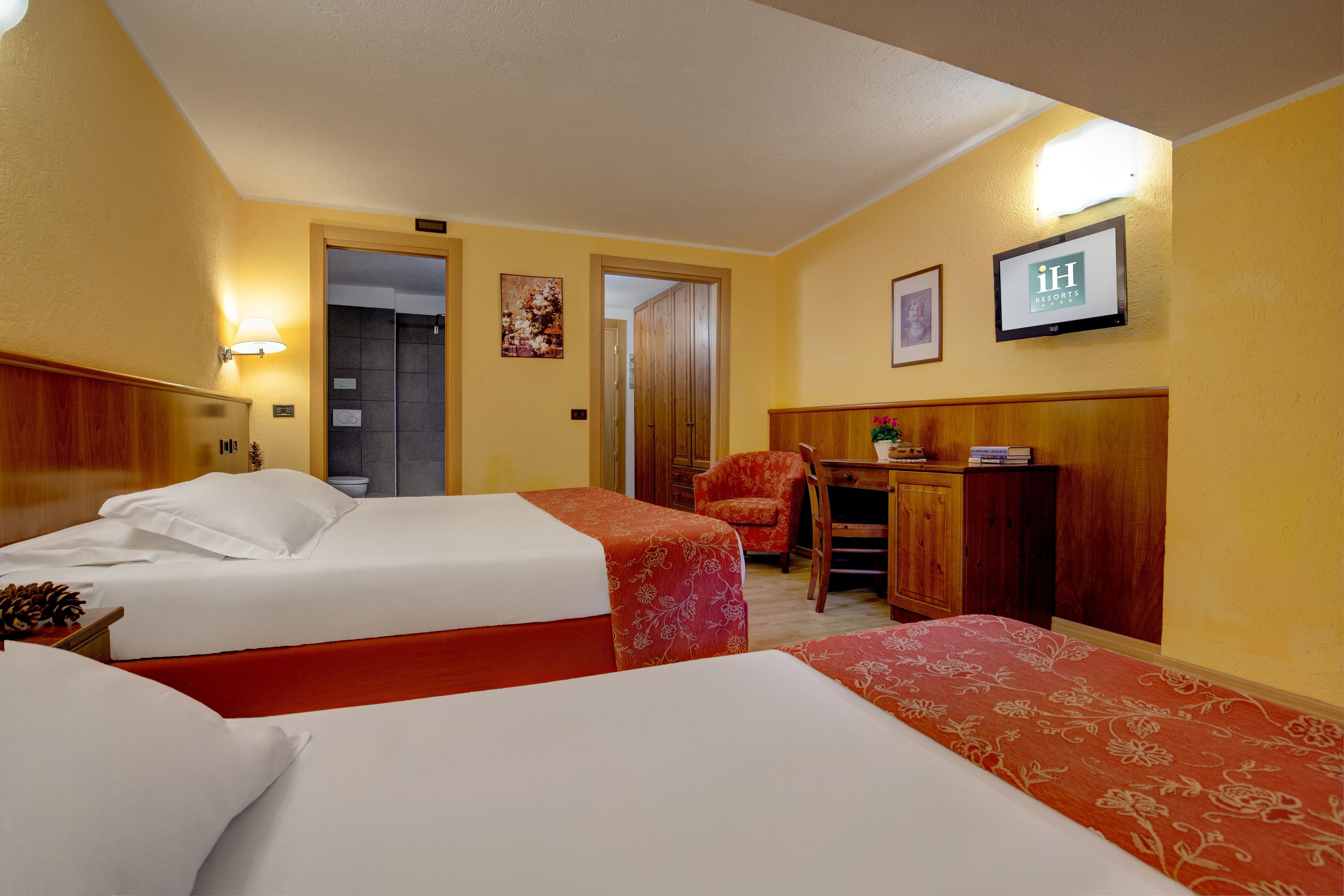 A hotel room with two beds, a desk, a chair, and a television on the wall.