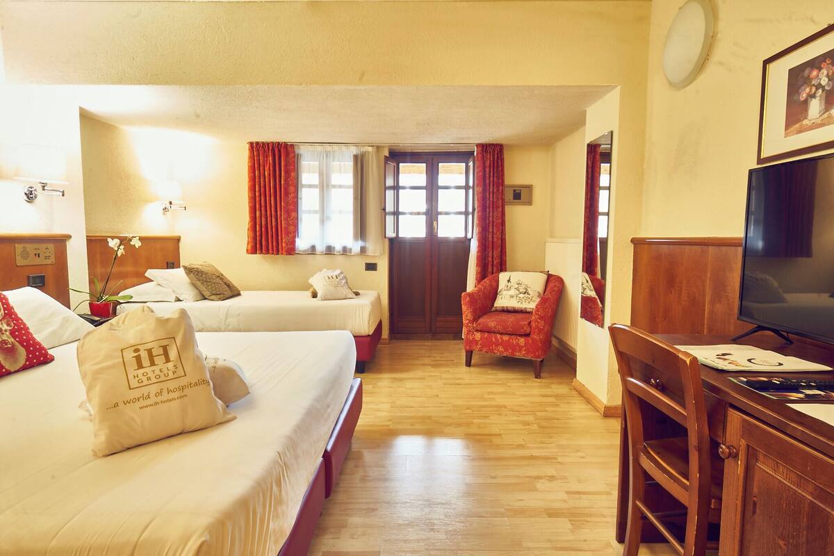 A hotel room with two beds, a desk, a chair, a TV, and a window with curtains.