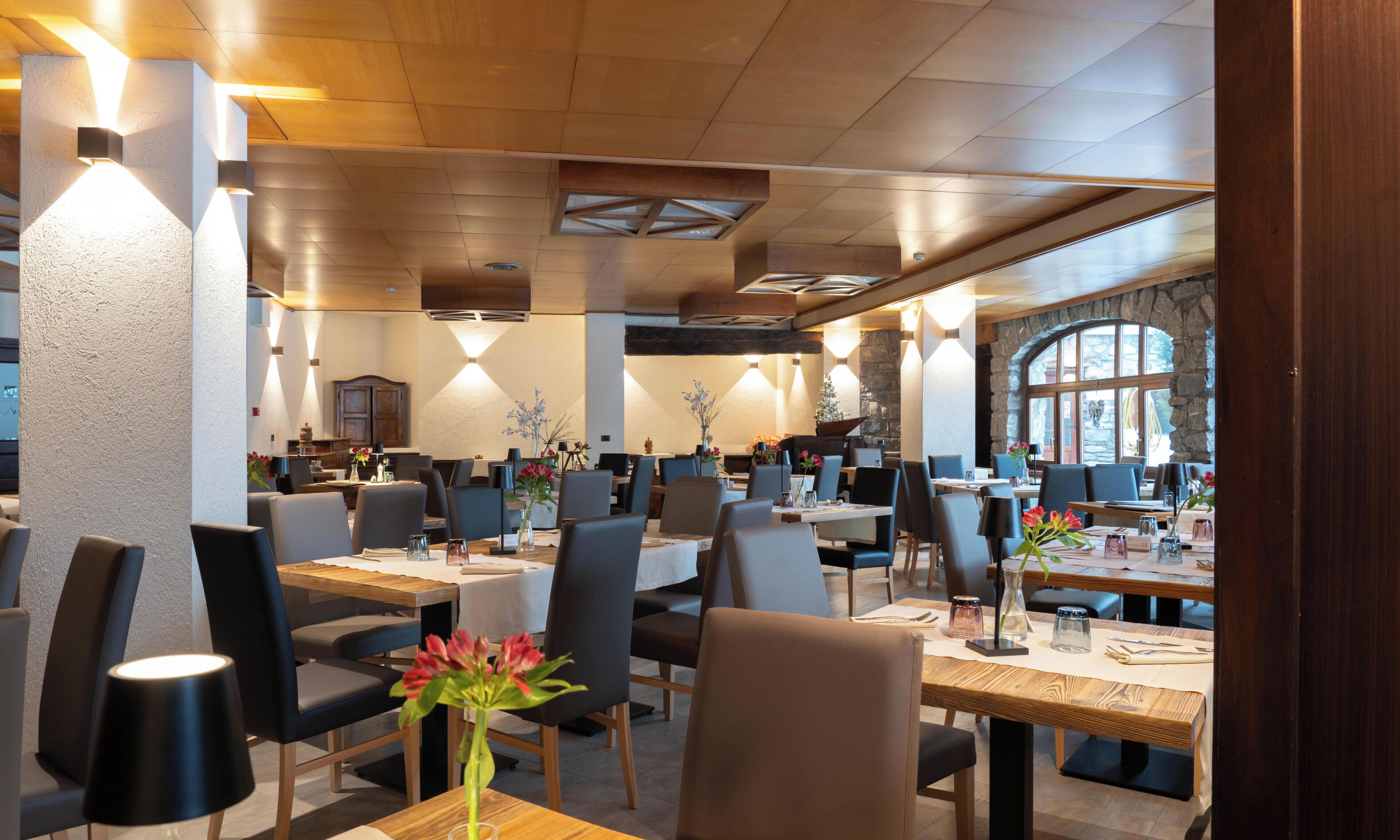 Un restaurante con varias mesas, sillas y una pared de piedra con ventanas.