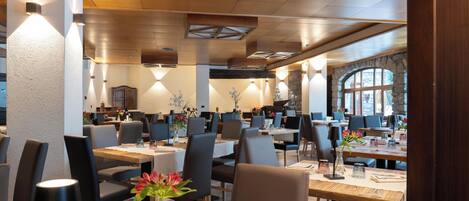 A restaurant with multiple tables, chairs, and a stone wall with windows.