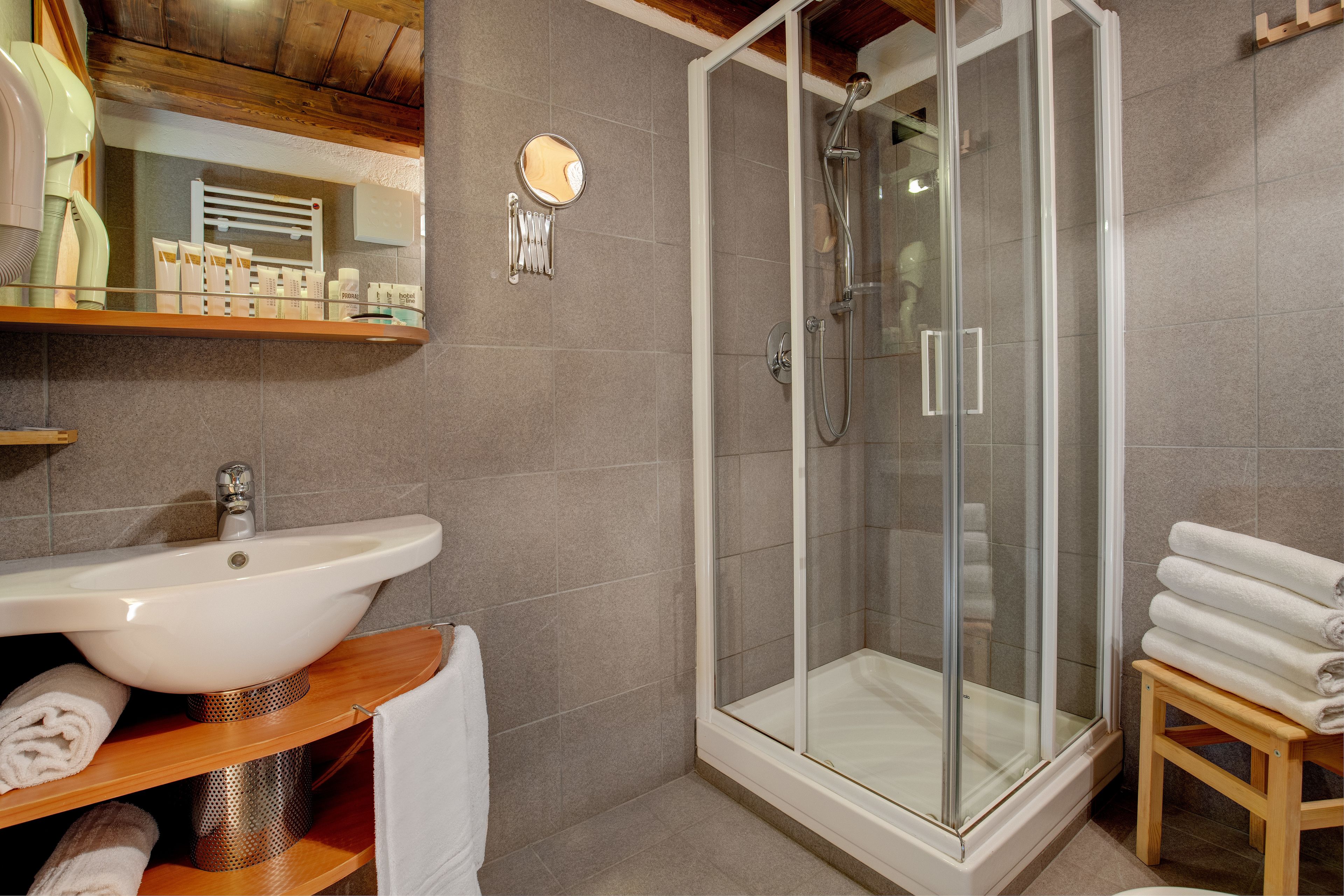 A bathroom with a glass-enclosed shower, a sink, and a wooden shelf with towels.