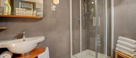 A bathroom with a glass-enclosed shower, a sink, and a wooden shelf with towels.