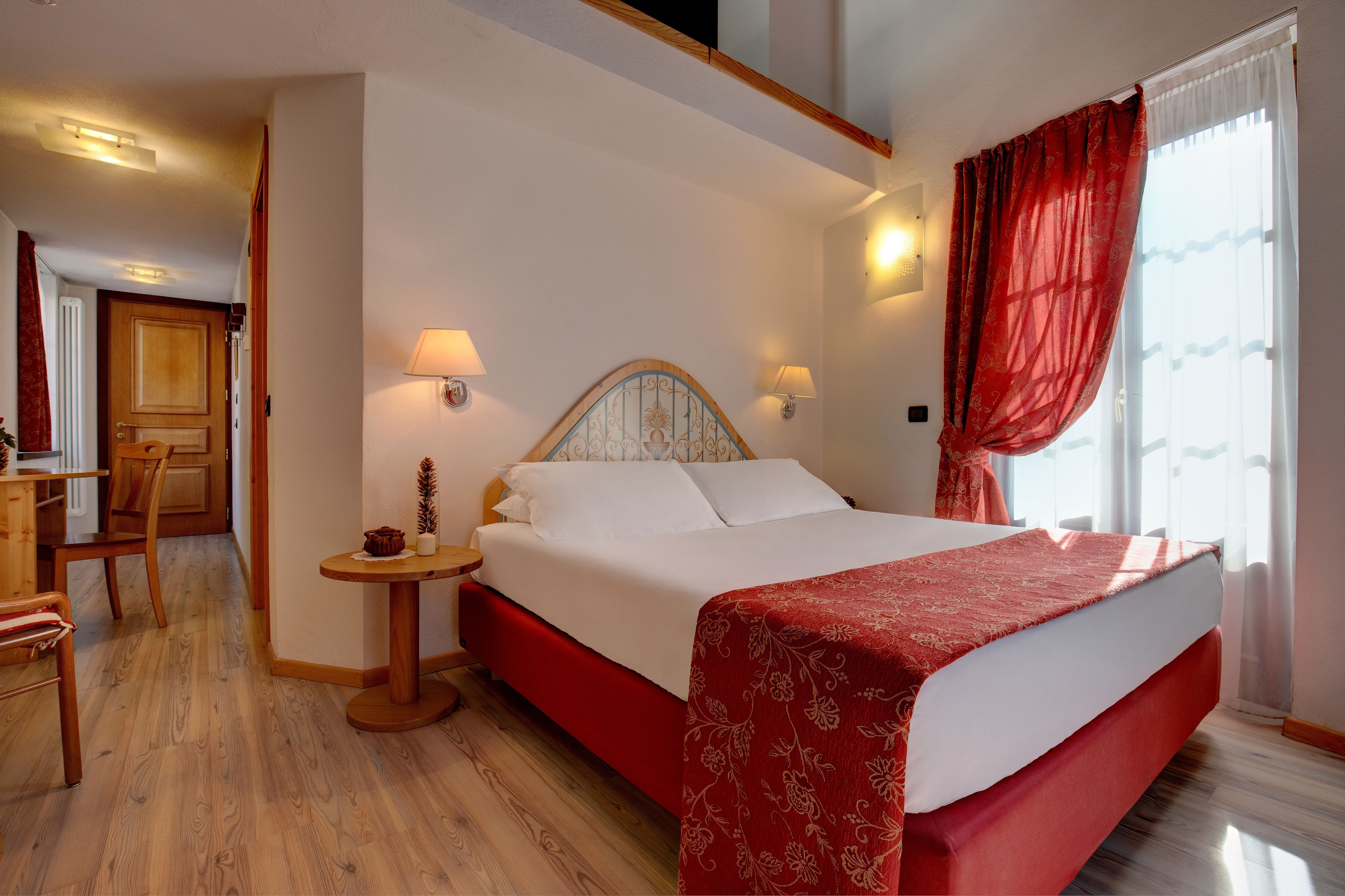 Una camera d'albergo con un letto, un comodino, una lampada e una finestra con tende.