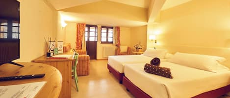 A hotel room with a desk, two beds, a chair, a window with curtains, and a radiator.