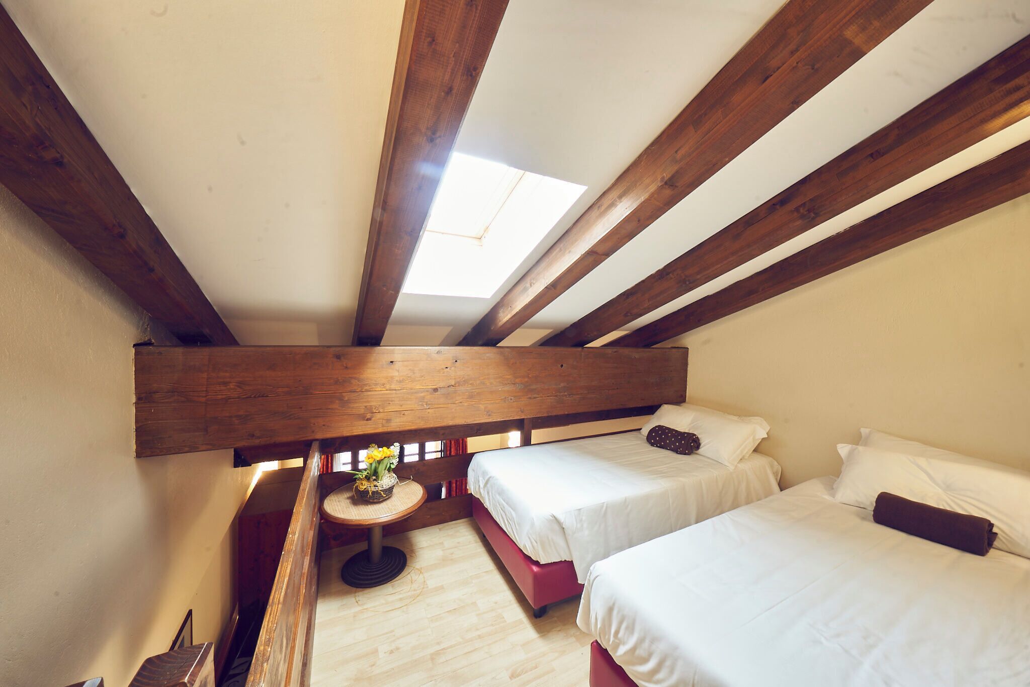 A room with two beds, a skylight, wooden beams, and a small table with flowers.