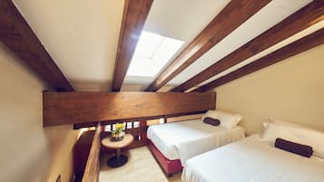 A room with two beds, a skylight, wooden beams, and a small table with flowers.