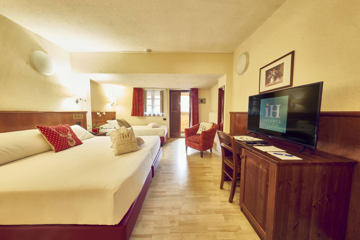 A hotel room with two beds, a desk, a television, and a chair.