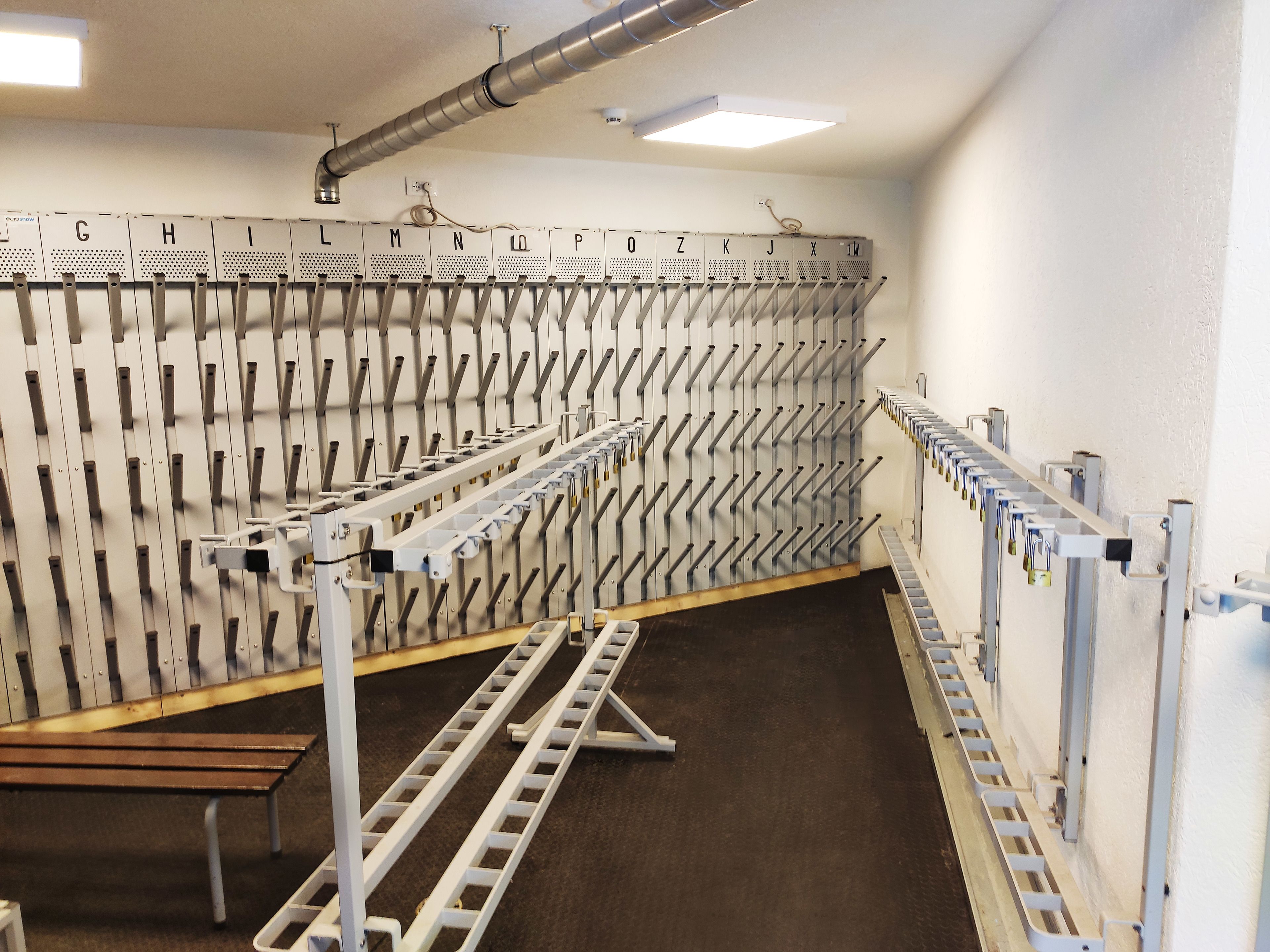 Een opslagruimte met metalen rekken voorzien van letters, een houten bankje en een ventilatiesysteem.