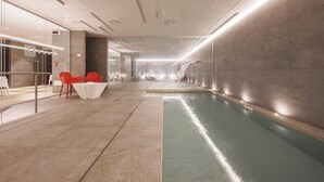 A modern indoor swimming pool area with a glass wall, red and white chairs, and a reception desk. - IH Hotels Courmayeur Mont Blanc Resort (Courmayeur)
