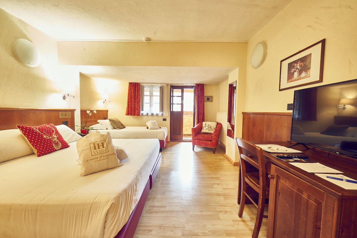 A hotel room with two beds, a desk with a TV, and a chair.