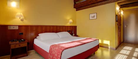 Une chambre d’hôtel avec une tête de lit en bois, un lit recouvert d’une courtepointe rouge et blanche, deux lampes de chevet, une table de chevet avec un téléphone et un plancher en bois.