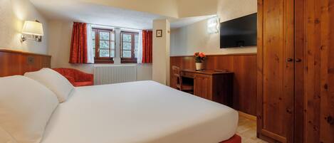 A hotel room with a large bed, a desk, a chair, a TV, and wooden wardrobe.