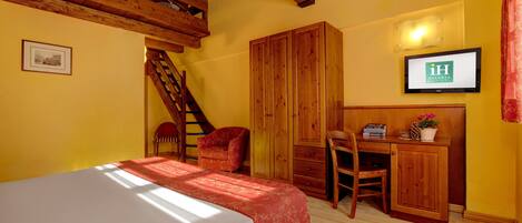 A bedroom with a bed, wooden wardrobe, desk, chair, and a TV on the wall.