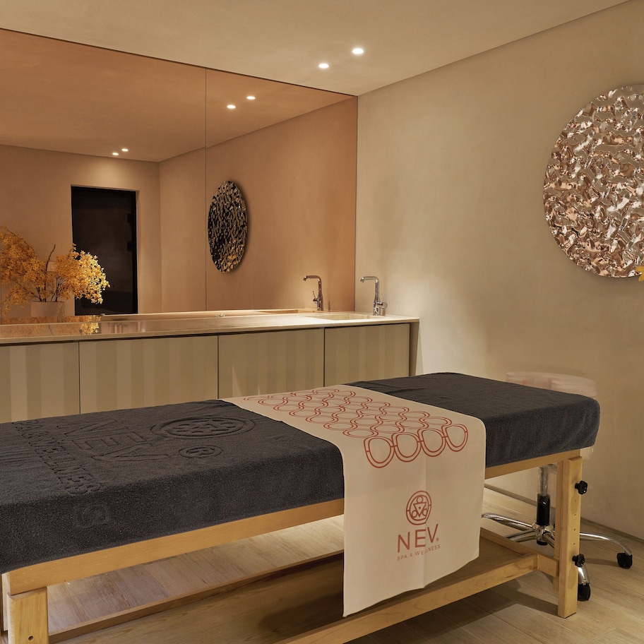 A modern spa room with a massage table, a large mirror, and a decorative wall piece.