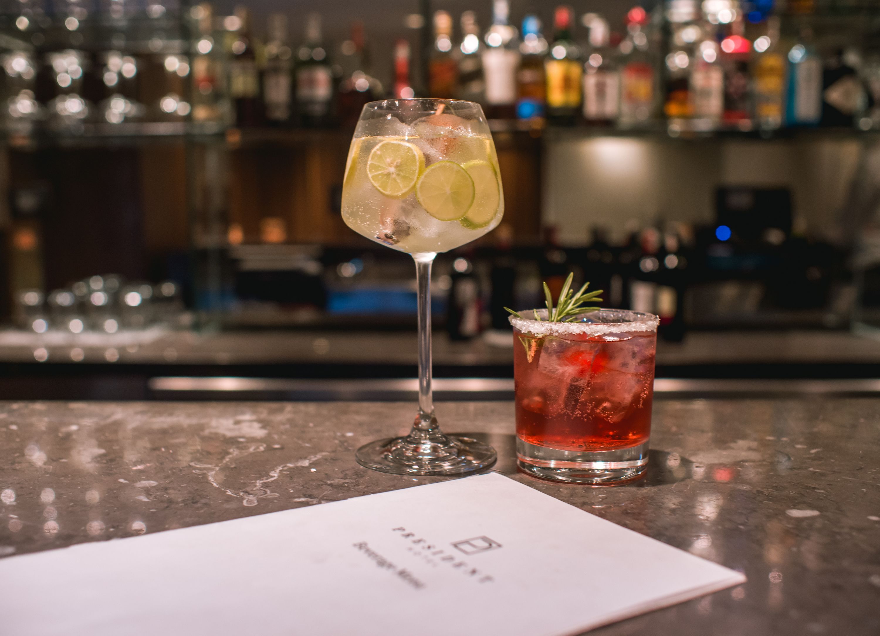 A bar setting with two drinks, one in a tall glass and one in a short glass, with a menu in front.