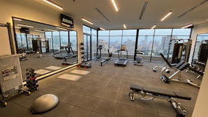 A modern gym with various exercise equipment, large windows offering a city view, and a mirror reflecting the space. - The President Hotel Cairo (Cairo)