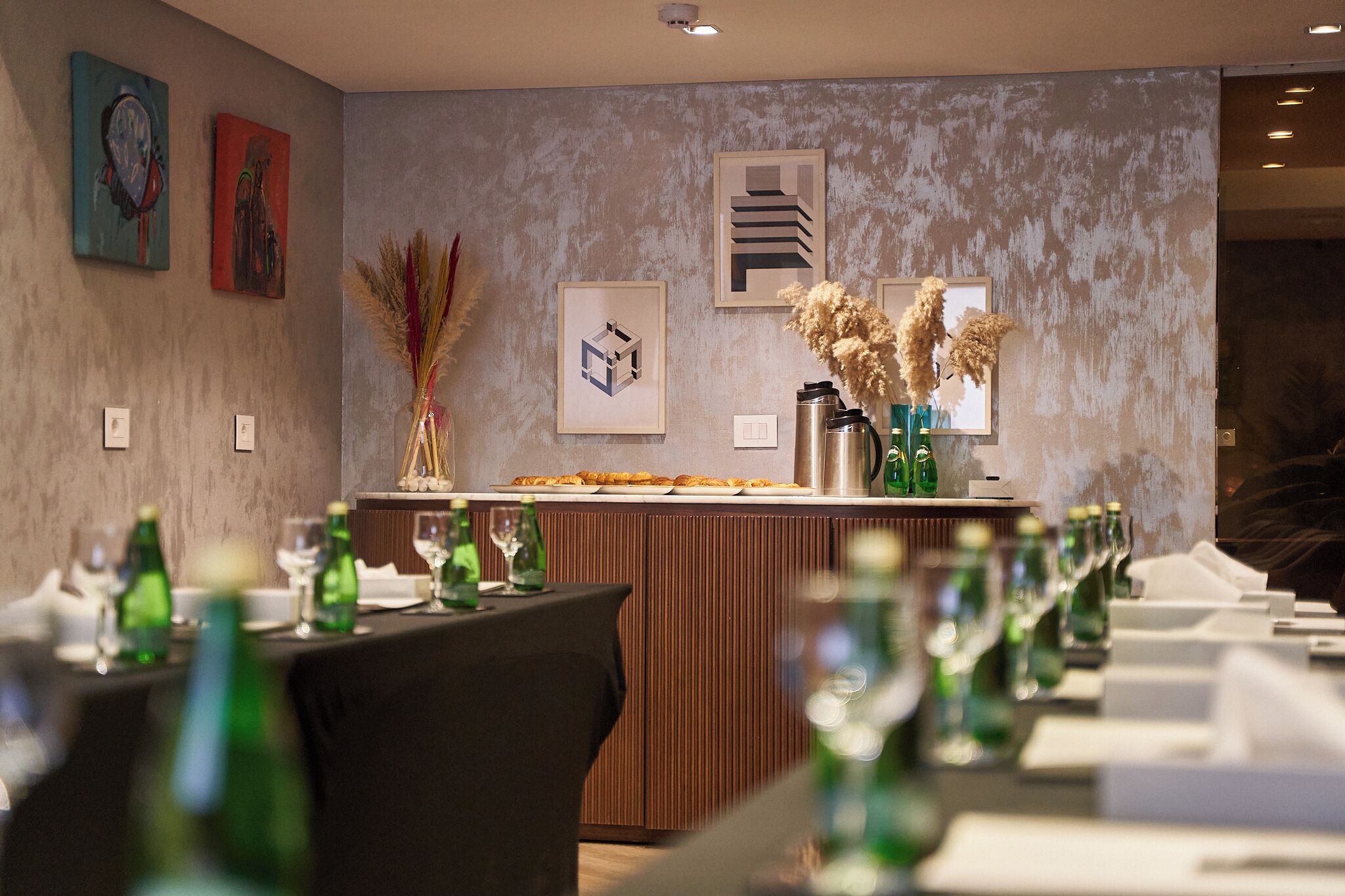 A restaurant with a long counter, green bottles, and framed artwork on the wall.