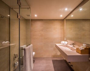 Un baño moderno con cabina de ducha de vidrio, un espejo grande y un tocador con lavamanos y espacio para toallas.