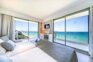 Quarto de hotel com uma cama grande, uma escrivaninha, uma televisão e varanda com vista para o mar.