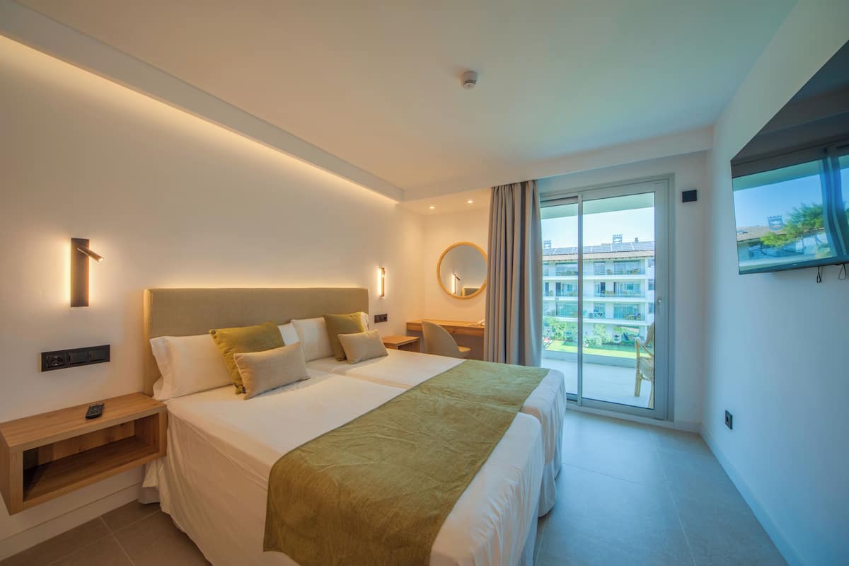 A modern hotel room with a large bed, a desk, a chair, a window, and a balcony.