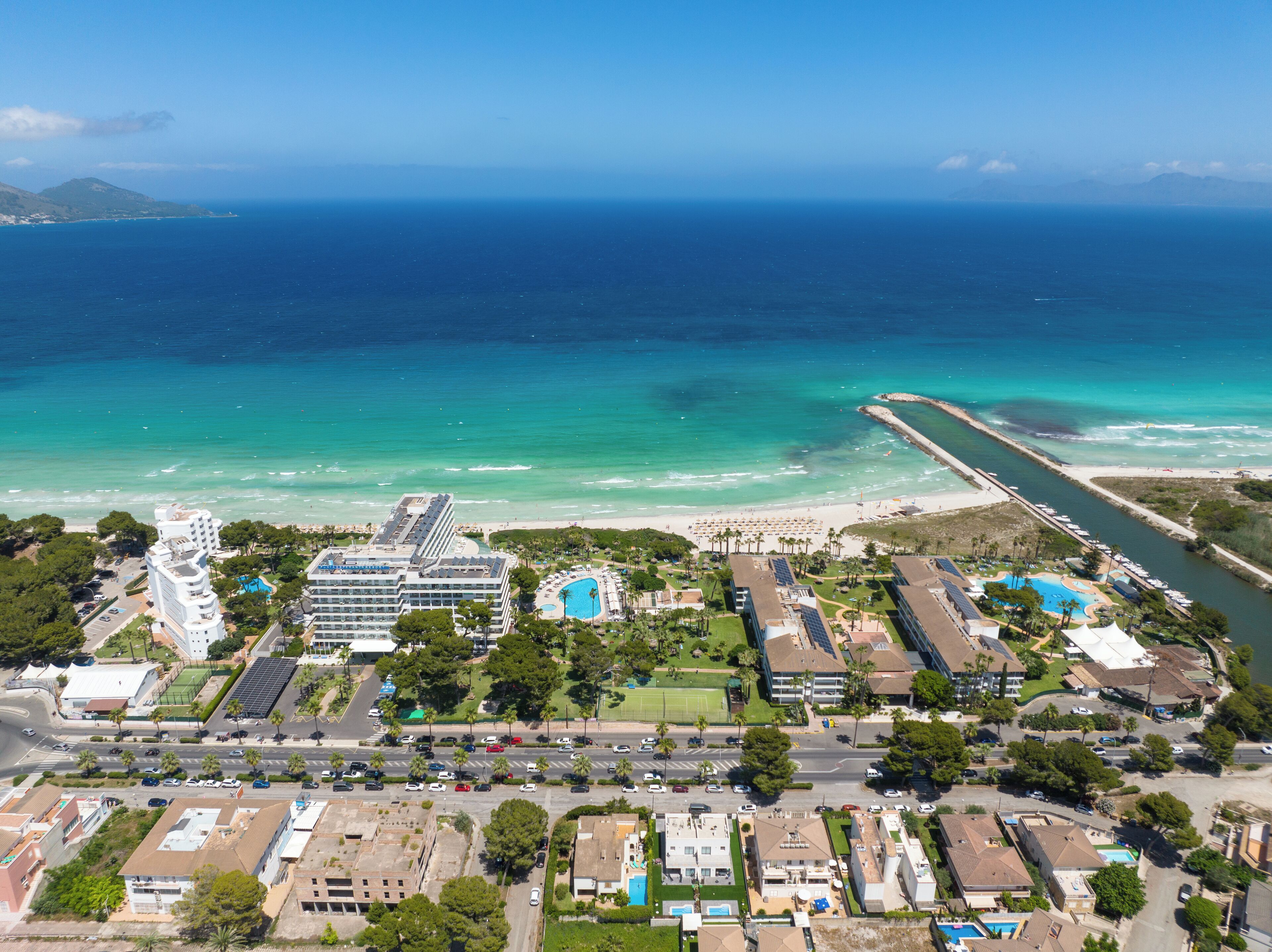 Ein Luftbild eines Küstenresorts mit Strand, einer Marina und einem Hotel mit mehreren Schwimmbecken.